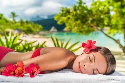 Rilassante donna che riceve massaggio wellness su spiaggia tropicale con fiori di ibisco.