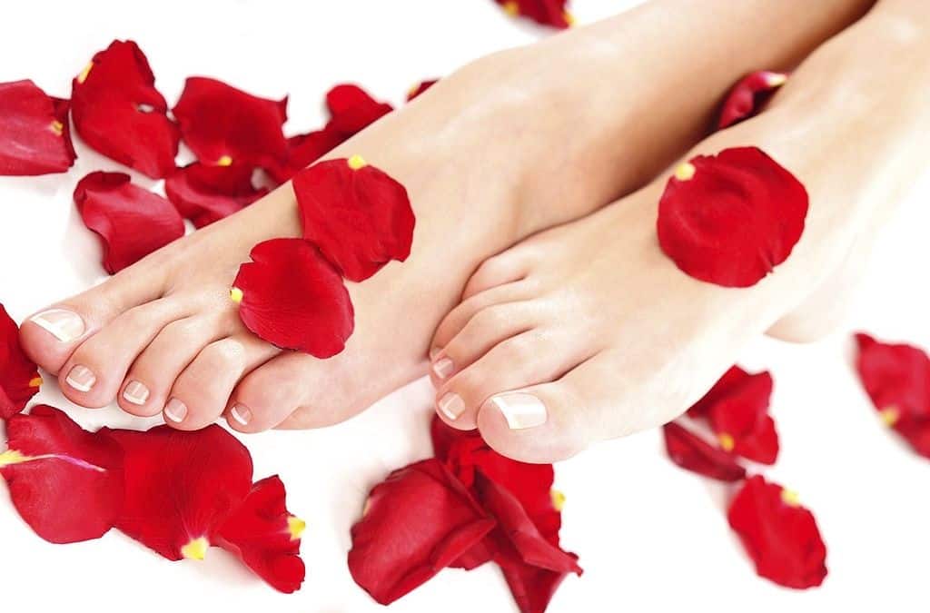 Cuore di piedi con petali di rosa rossi sparsi intorno, trattamenti benessere, cura del corpo, relax e bellezza.