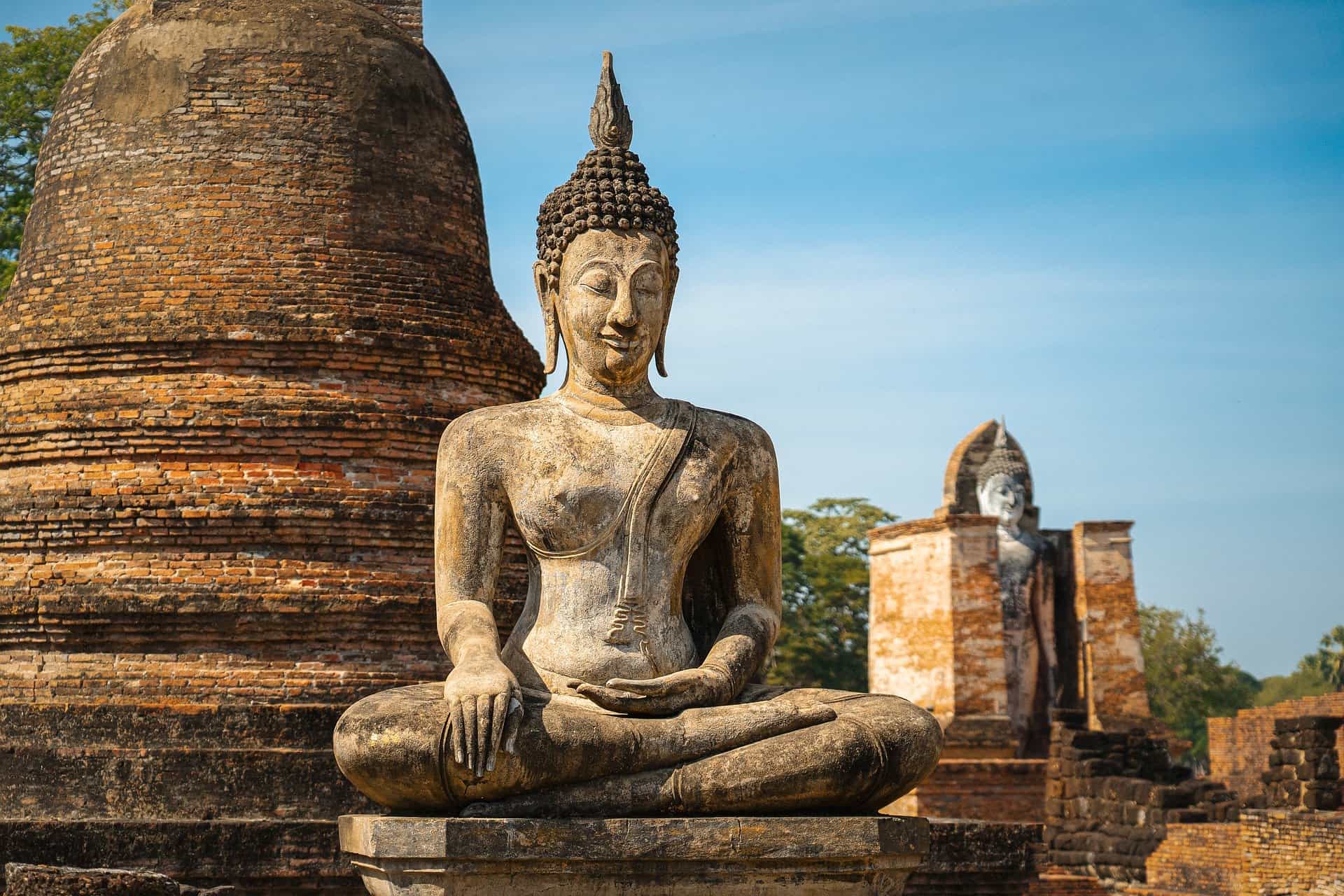 Statuetta di Buddha in piedi tra antichi templi di mattoni a Thailandia, simbolo di spiritualità e mindfulness.
