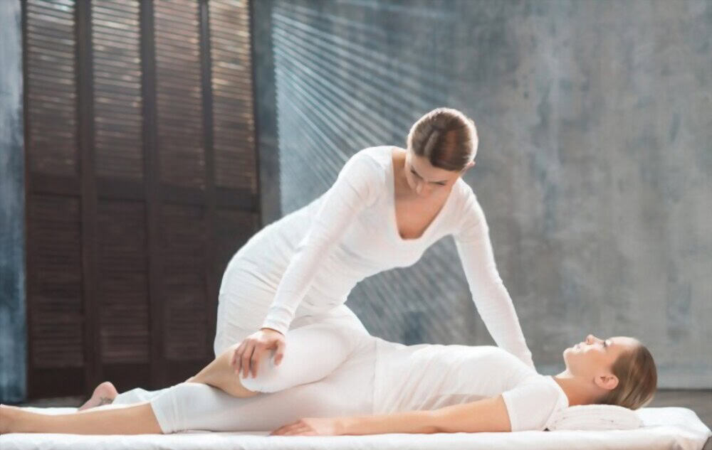 Massaggiatrice che esegue un massaggio rilassante a una paziente distesa su un futon, centro benessere, tecniche di massaggio naturale.