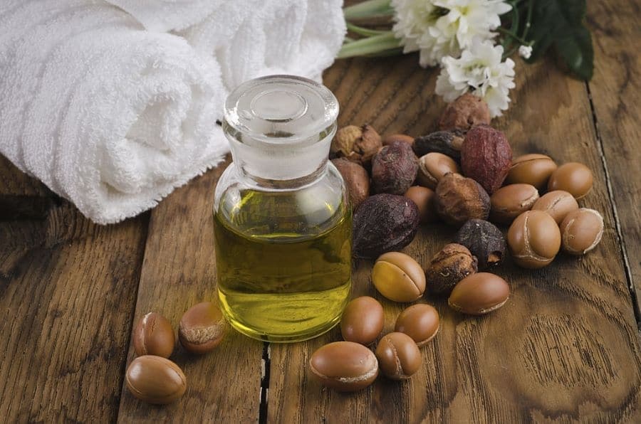 Olio di argan naturale con pietre e fiori su tavola in legno, benessere e relax, evoluzione nel benessere, Evolution Academy&reg;.
