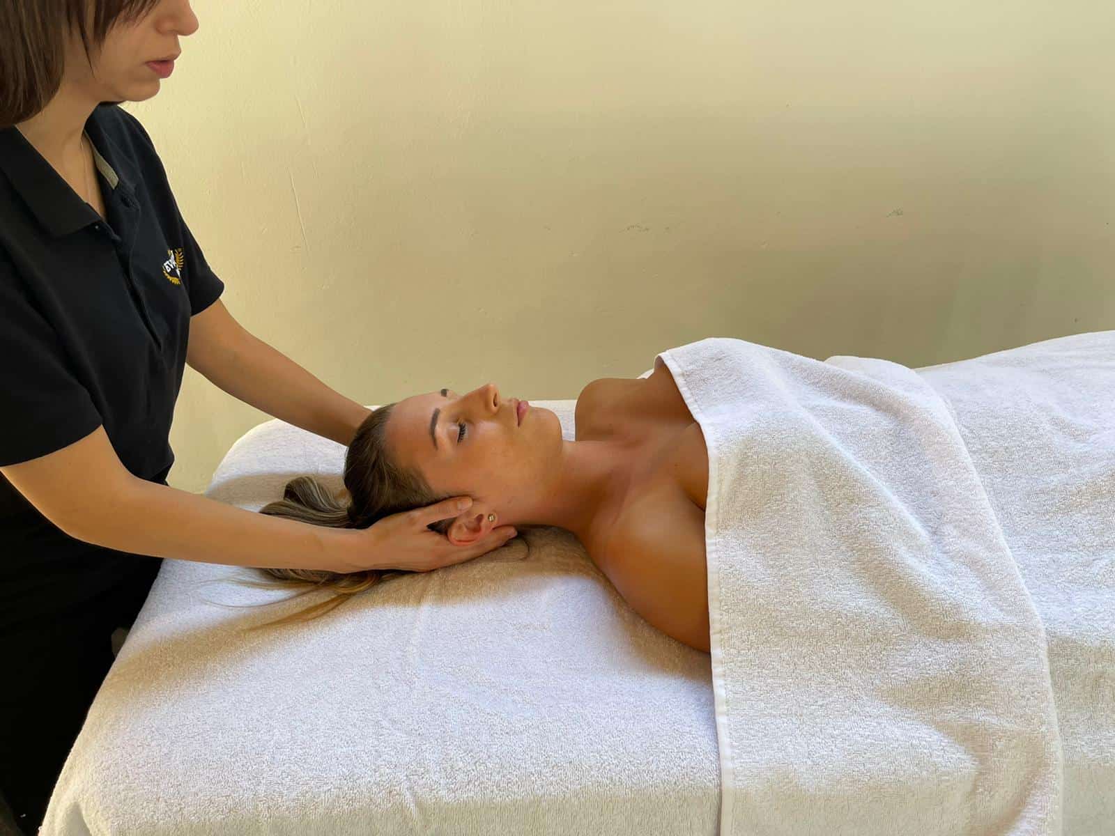 Massaggiatrice che massaggia il collo di una donna sdraiata su un lettino, una sessione di benessere e terapia naturale.