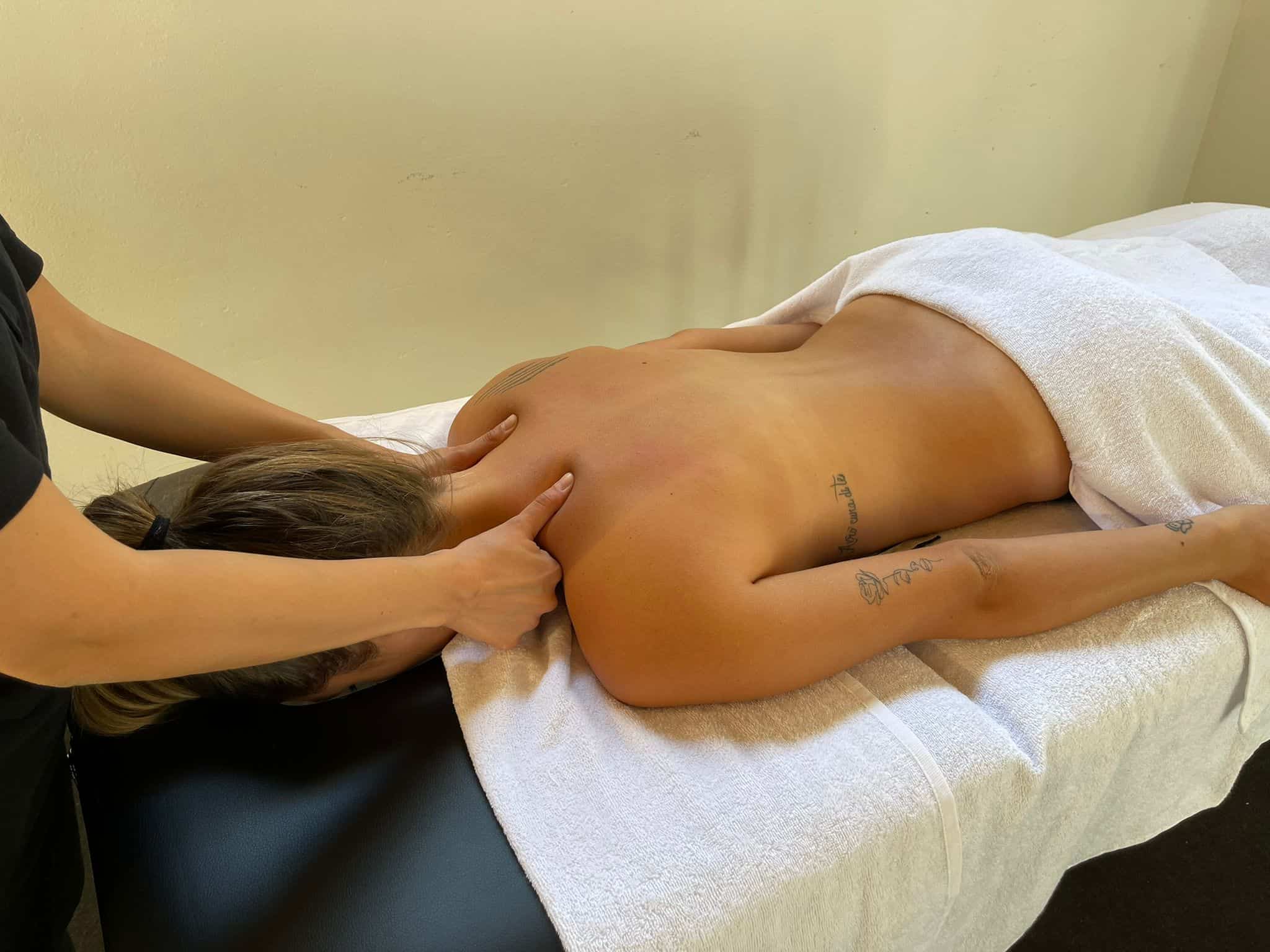 Tecnico di massaggi professionista che lavora sulla schiena e le spalle di una cliente su un tavolo da massaggi.