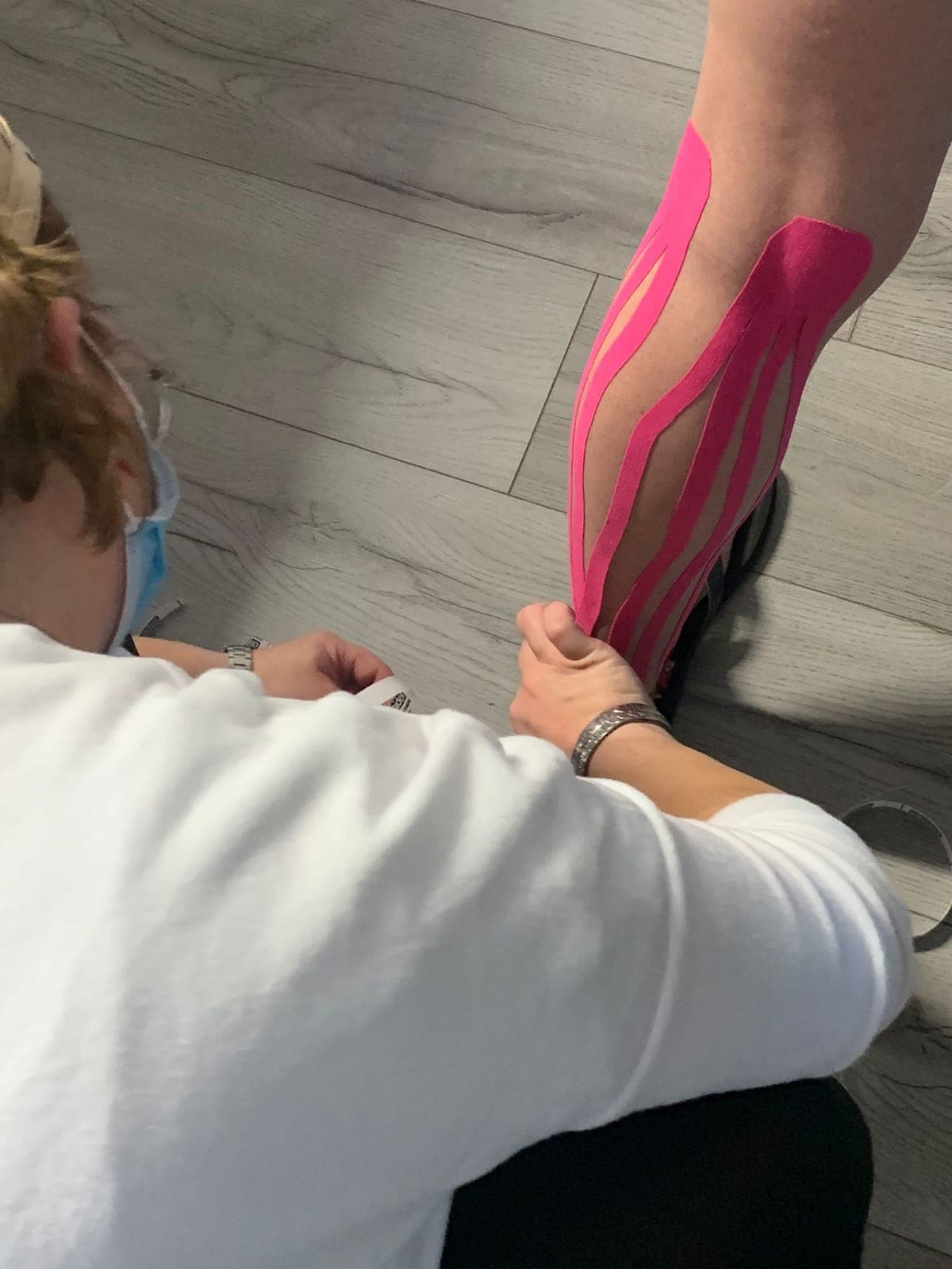 Guida applica kinesio tape su gamba di una donna, tecnica di riabilitazione sportiva e benessere fisico.