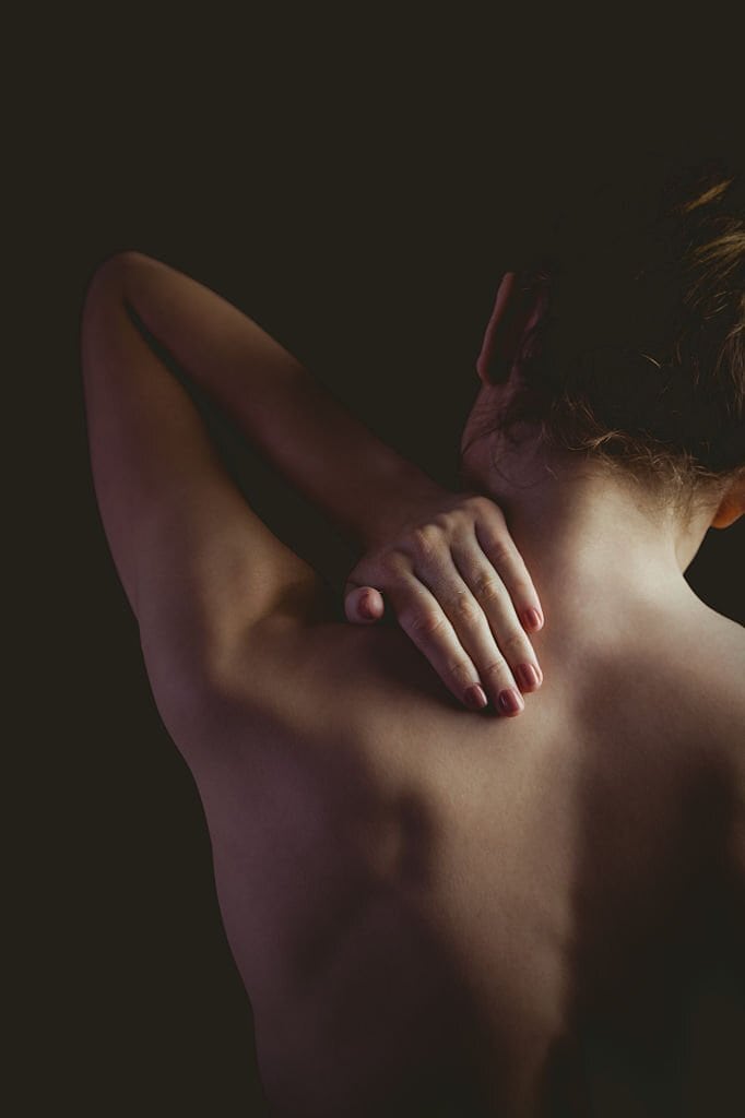 Corpo femminile in posa di relax con mano sulla spalla, espressione di benessere e consapevolezza corpo.