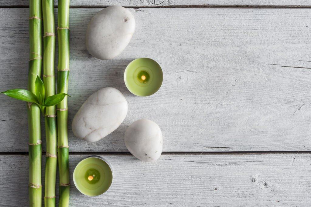 Bambù, pietre e candele verdi su tavola di legno chiaro.